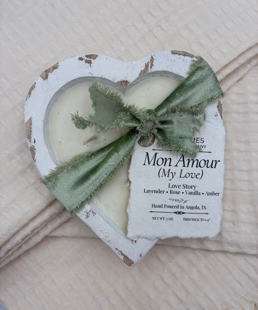 Two heart-shaped candles with a green ribbon on a textured surface