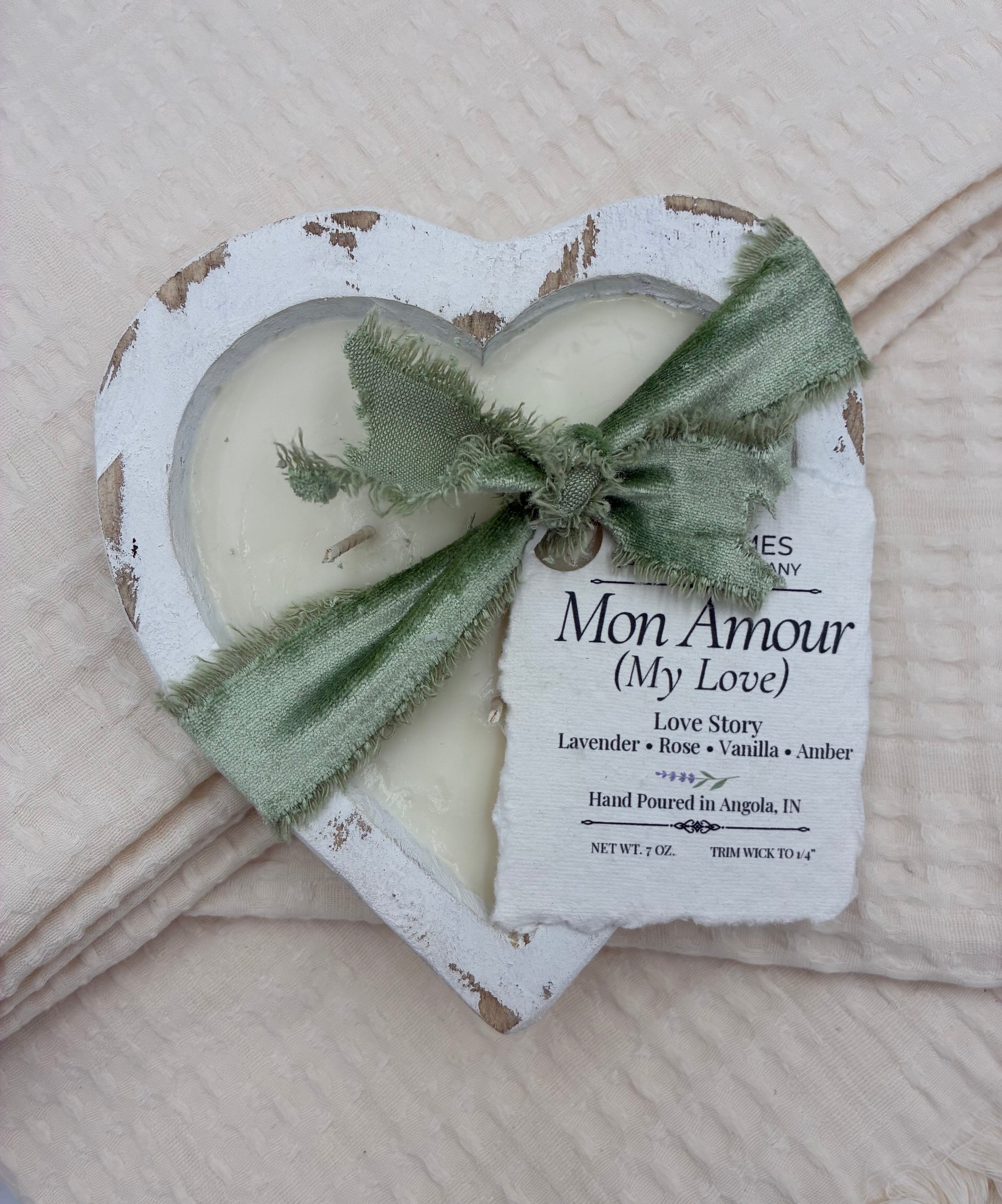 Two heart-shaped candles with a green ribbon on a textured surface