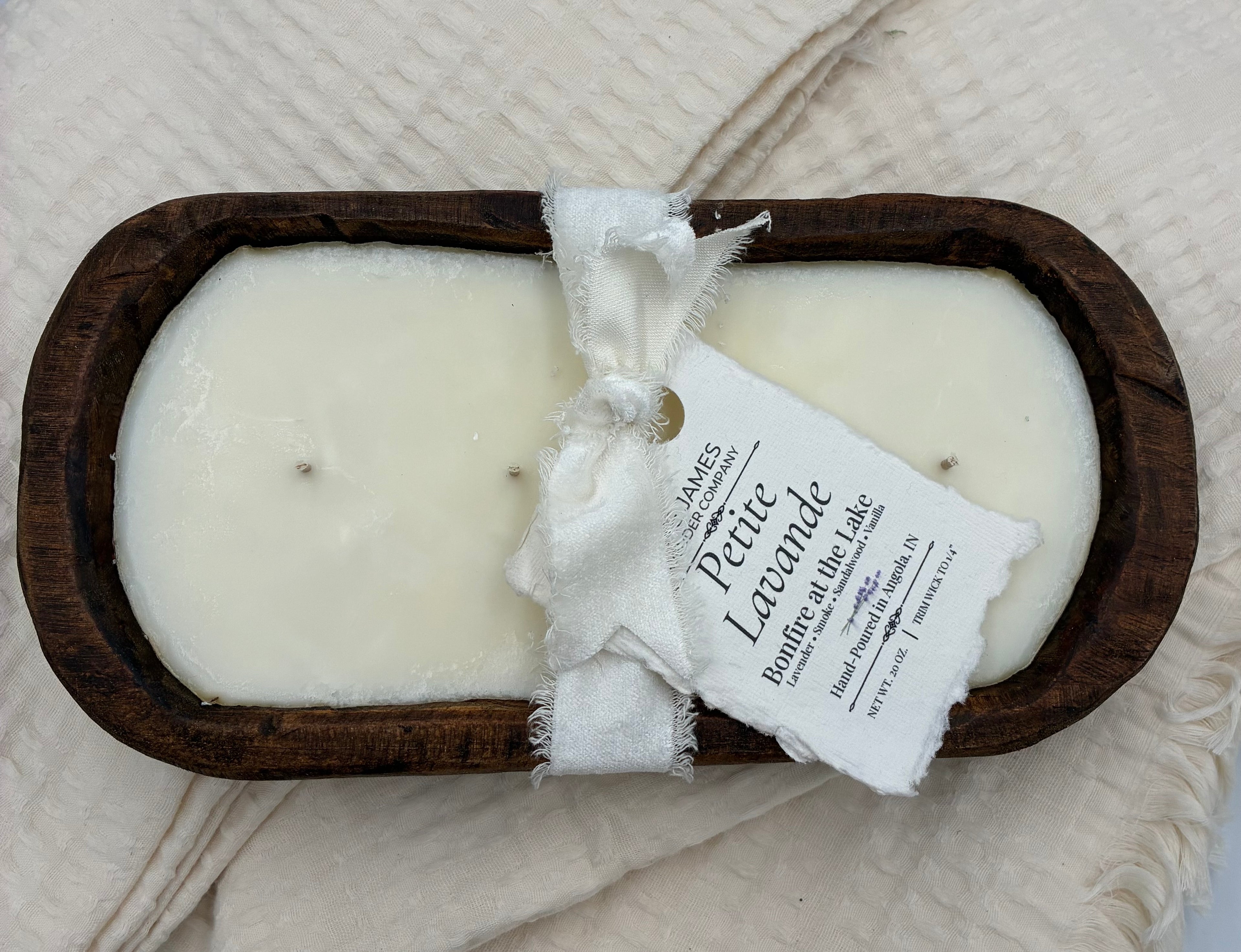 Two white candles in a wooden dish with a label on a textured surface